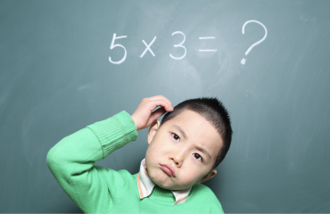 A young boy wearing a green jumper ponders a maths division question