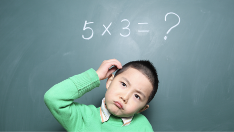 A young boy wearing a green jumper ponders a maths division question